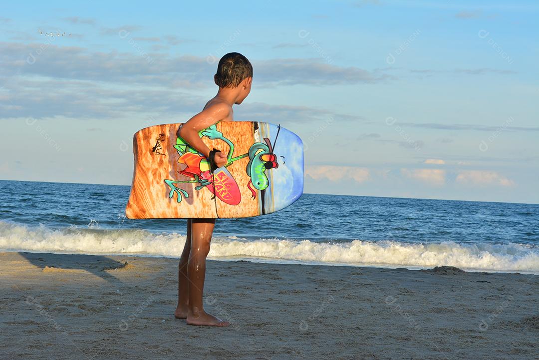 Menino segurando uma prancha na praia