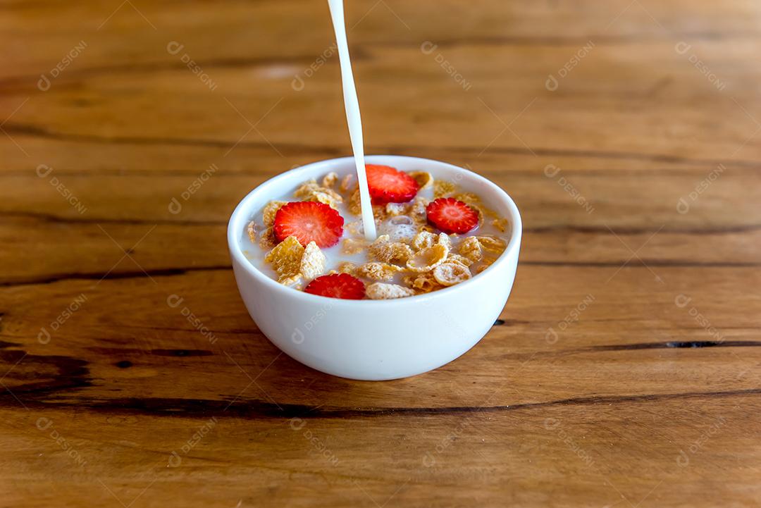 Derramando leite em flocos de milho com pedaços de morango, café da manhã com leite e flocos de milho