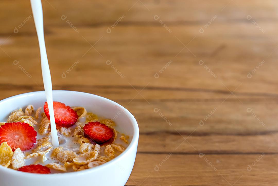 Derramando leite em flocos de milho com pedaços de morango, café da manhã com leite e flocos de milho