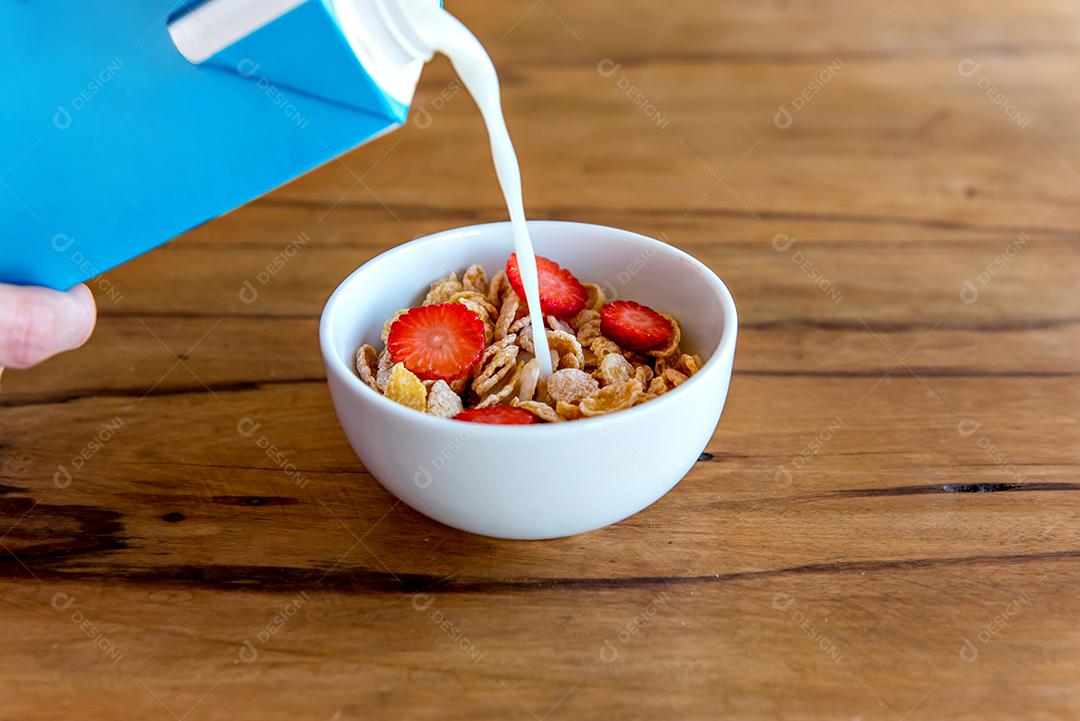 Derramando leite em flocos de milho com morango, café da manhã com leite e flocos de milho