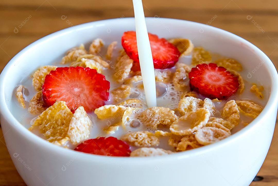 Derramando leite em flocos de milho com morango, café da manhã com leite e flocos de milho