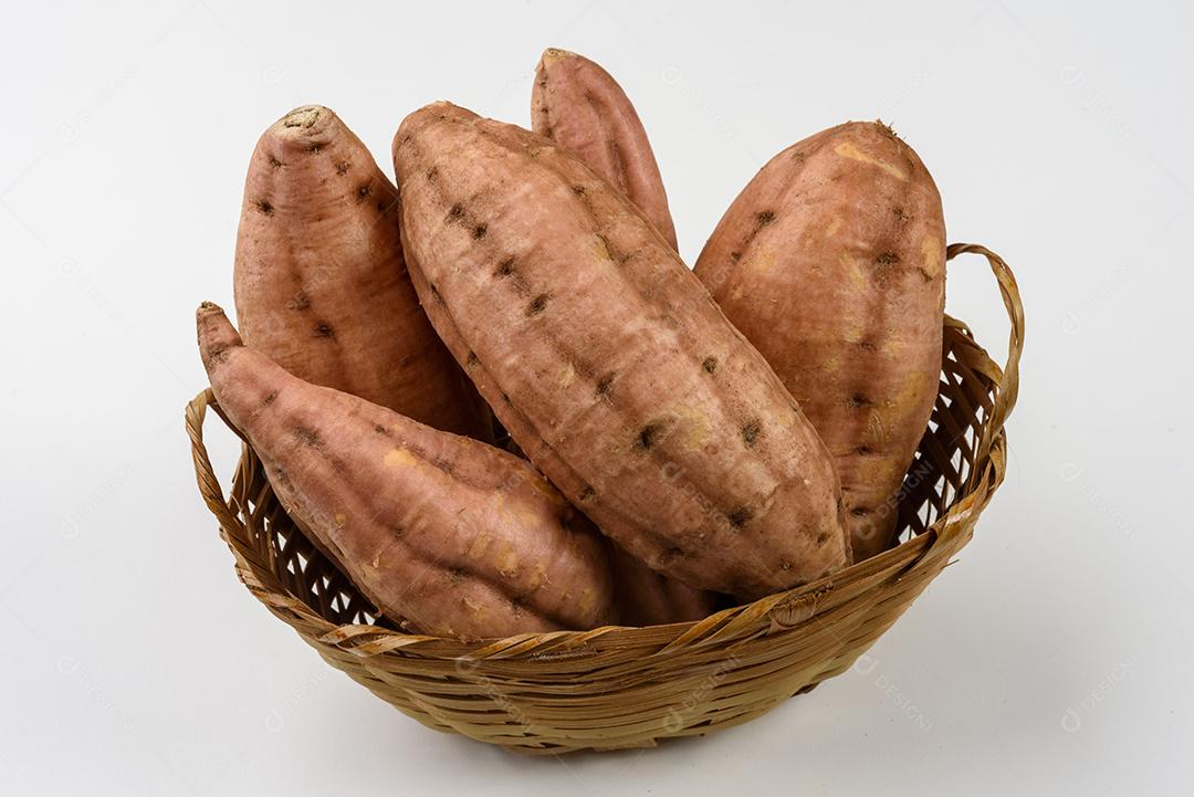 Cesta de palha com batatas doces cruas dentro em fundo branco