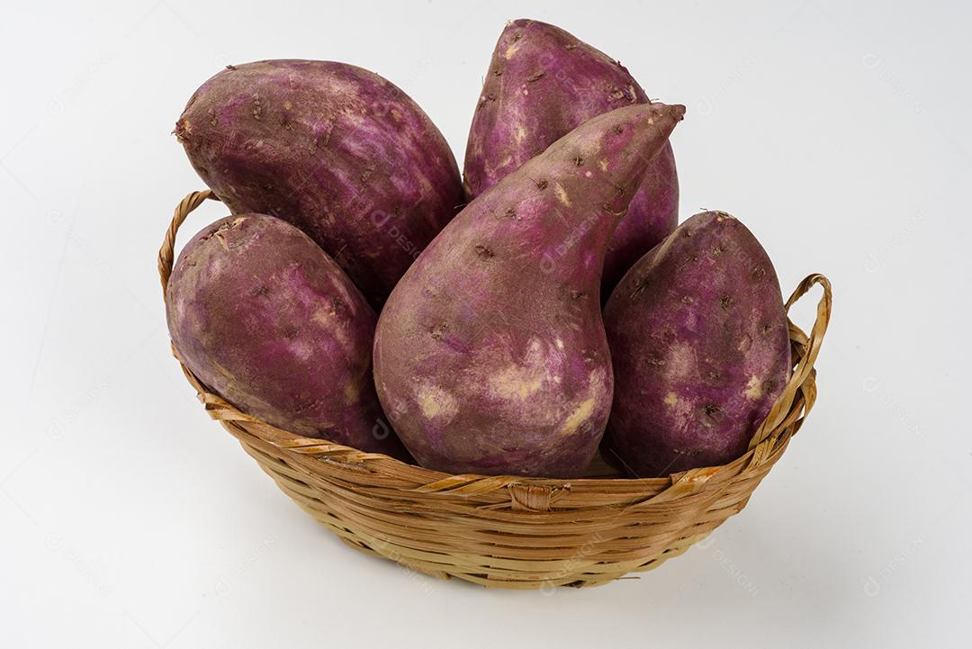 Cesta de palha com batatas doces cruas dentro em fundo branco