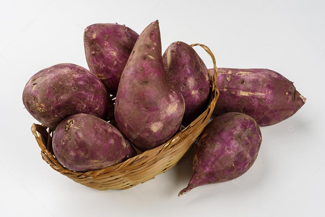 Cesta de palha com batatas doces cruas dentro em fundo branco