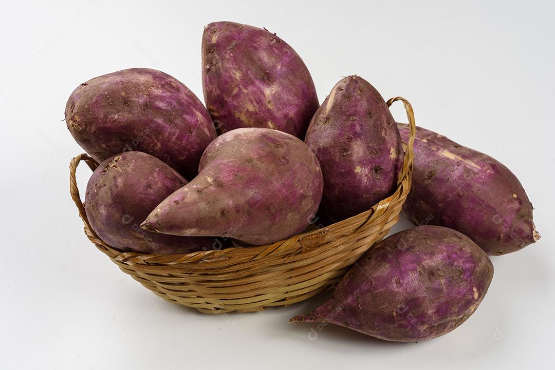 Cesta de palha com batatas doces cruas dentro em fundo branco