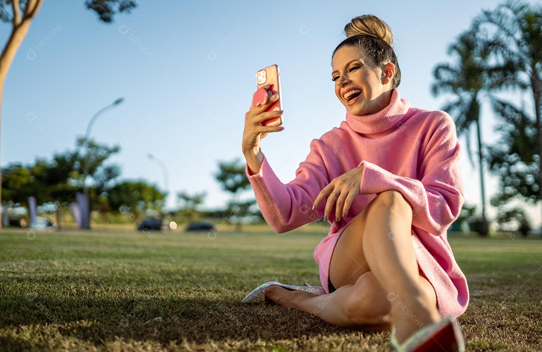 Imagem de uma jovem loira latina animada feliz usando o celular no fundo do parque