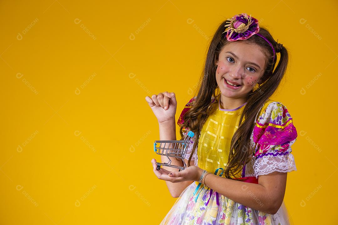linda garota caucasiana com roupa de festa junina segurando um mini carrinho de compras. Conceito de ecommerce e festa junina