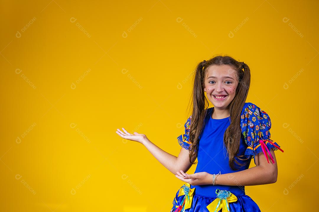 Criança com roupas típicas da famosa festa brasileira chamada Festa Junina em comemoração ao São João. Linda garota em fundo amarelo.