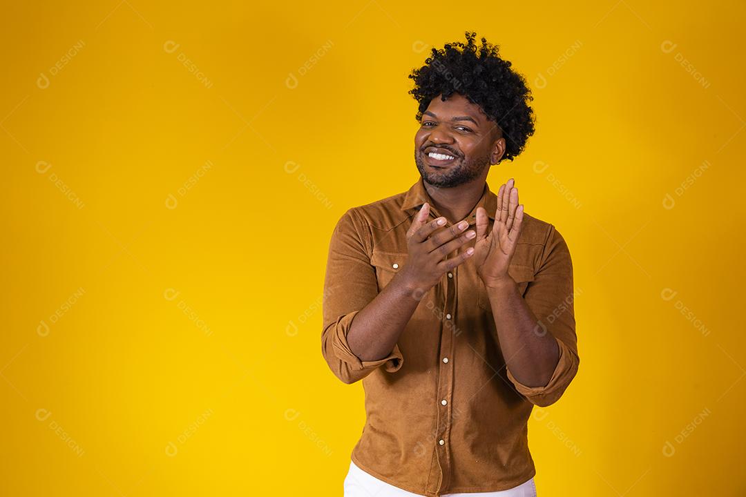 Jovem negro se sentindo feliz e bem sucedido, sorrindo e batendo palmas, dizendo parabéns com aplausos.