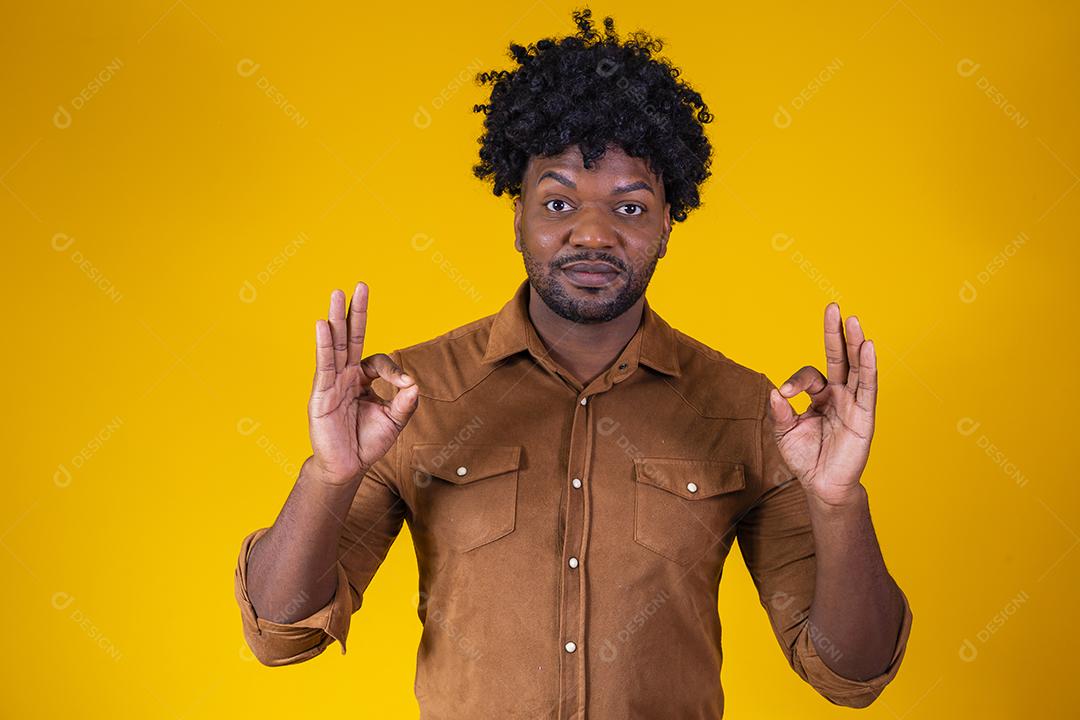 Retrato de homem negro feliz mostrando sinal de ok e sorrindo, sobre fundo amarelo