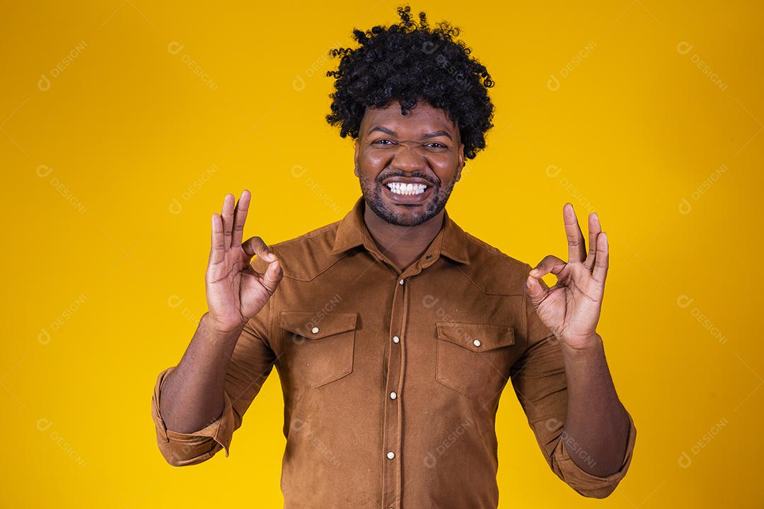 Retrato de homem negro feliz mostrando sinal de ok e sorrindo, sobre fundo amarelo