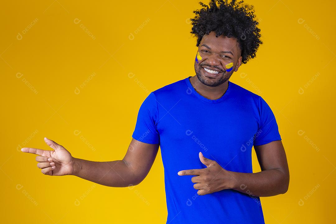 black man on yellow background with face painted in blue and yellow colors, pointing to the side