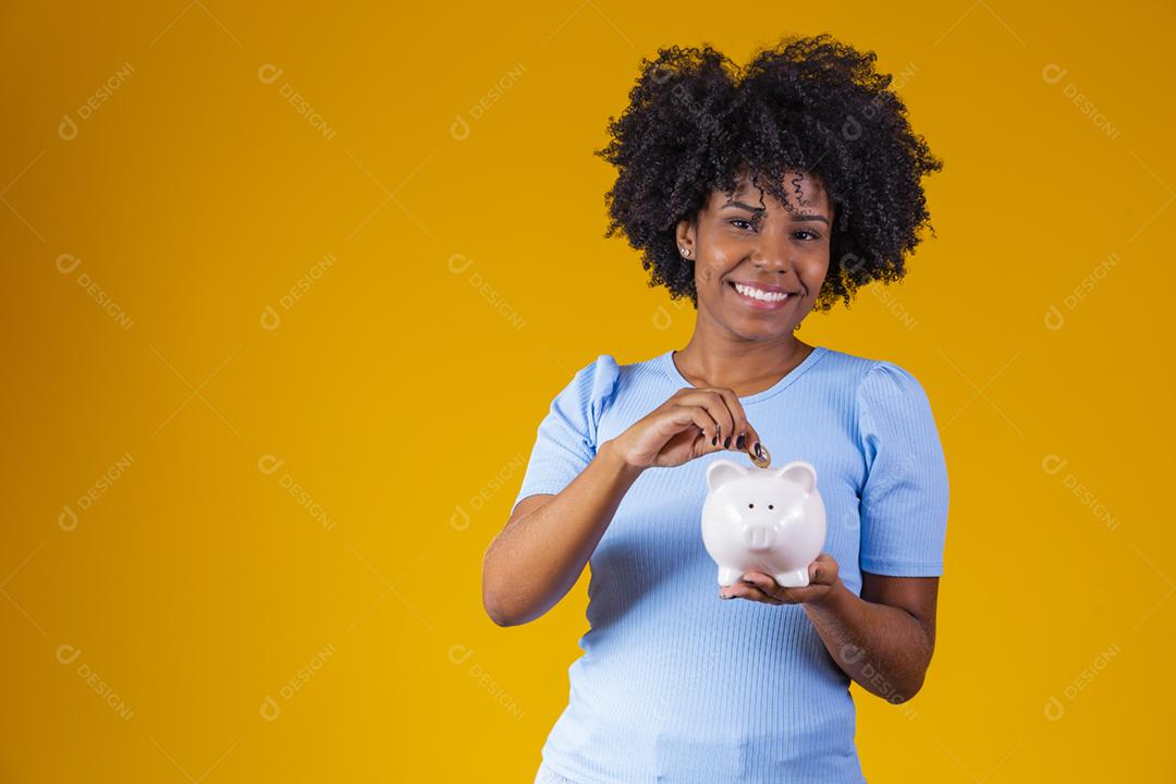 Mulher negra segurando um cofrinho. Mulher economizando dinheiro no porquinho