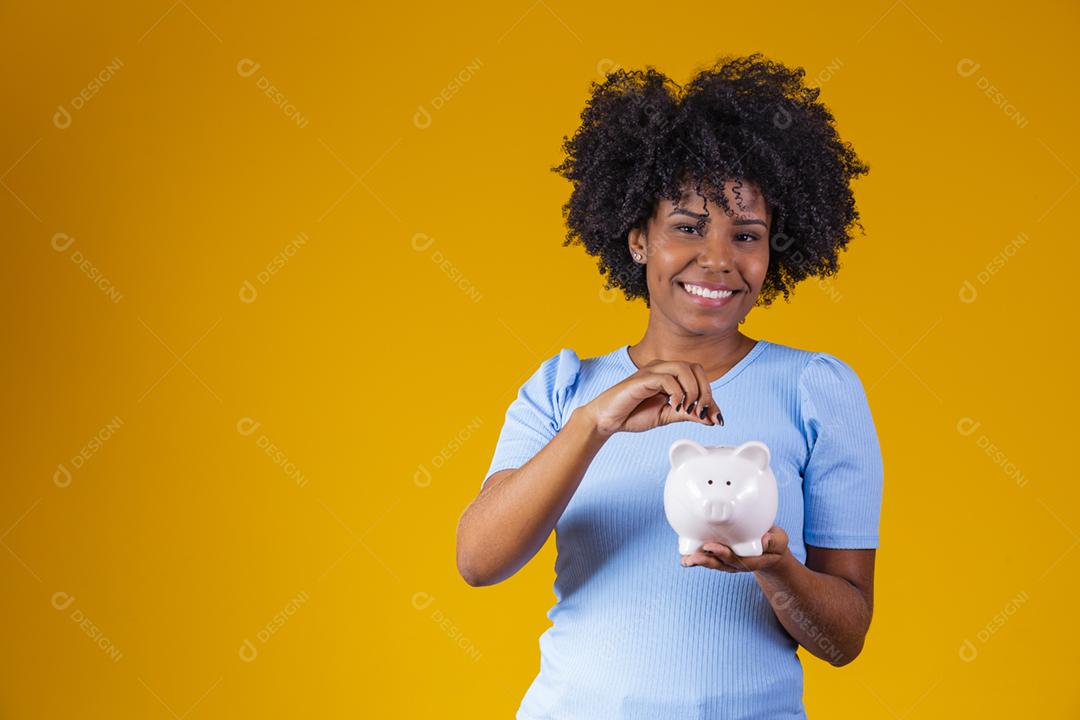 Mulher negra segurando um cofrinho. Mulher economizando dinheiro no porquinho