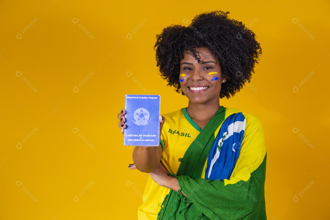 mulher afro brasileira segurando uma carteira de trabalho em fundo amarelo.