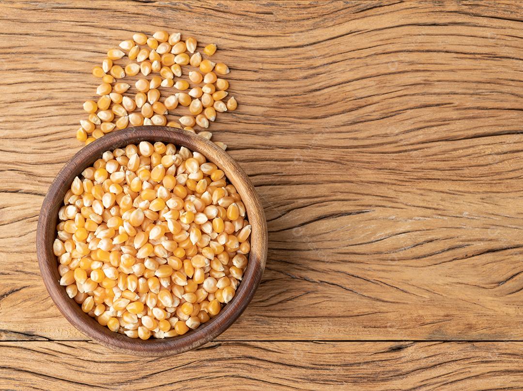 Grãos secos de milho ou pipoca em uma tigela sobre mesa de madeira com co