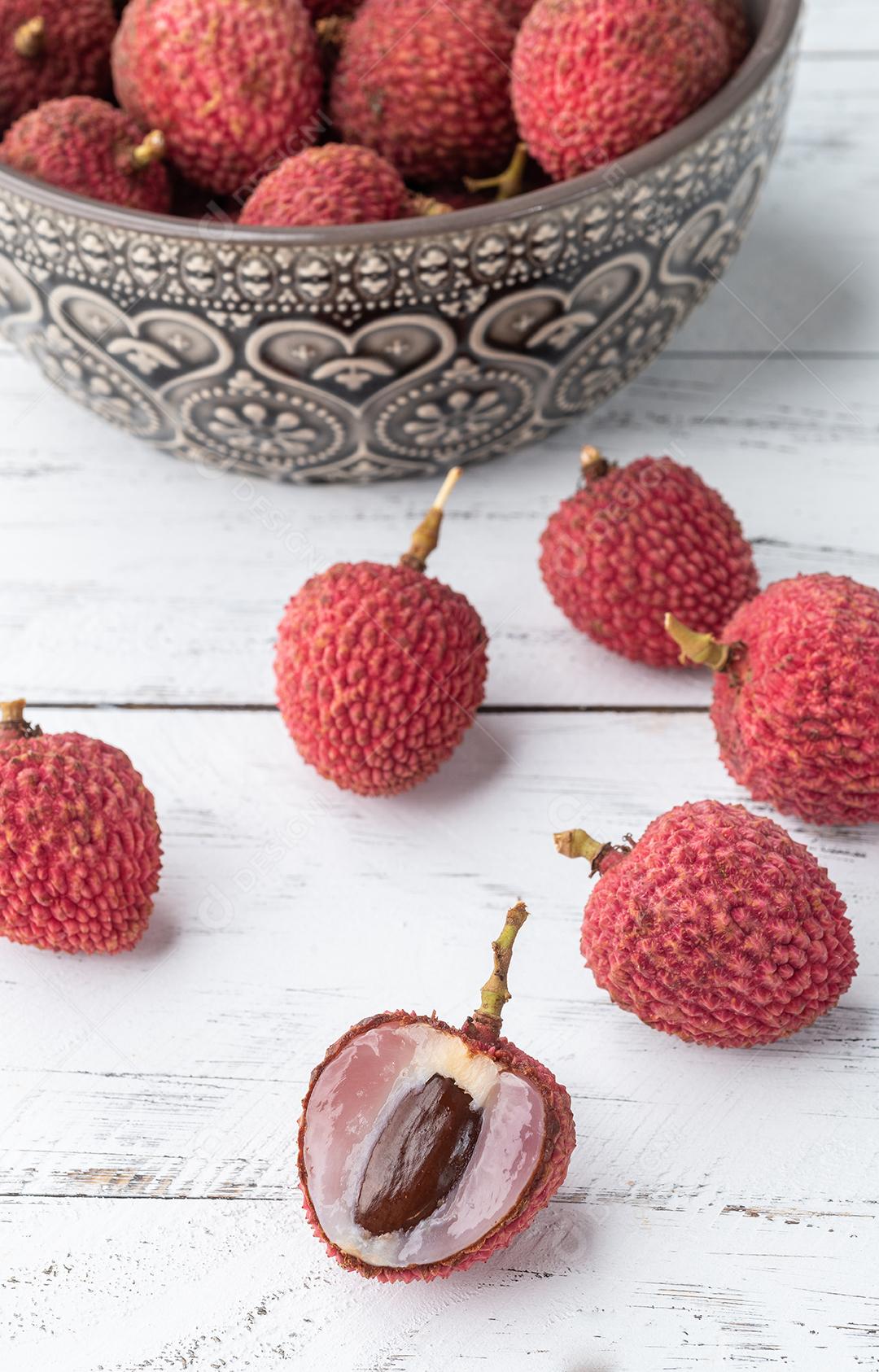 Lichias em uma tigela com frutas cortadas sobre a mesa de madeira