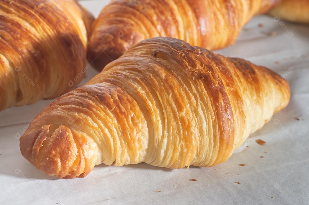 Deliciosos croissants caseiros em um papel manteiga branco, luz natural.
