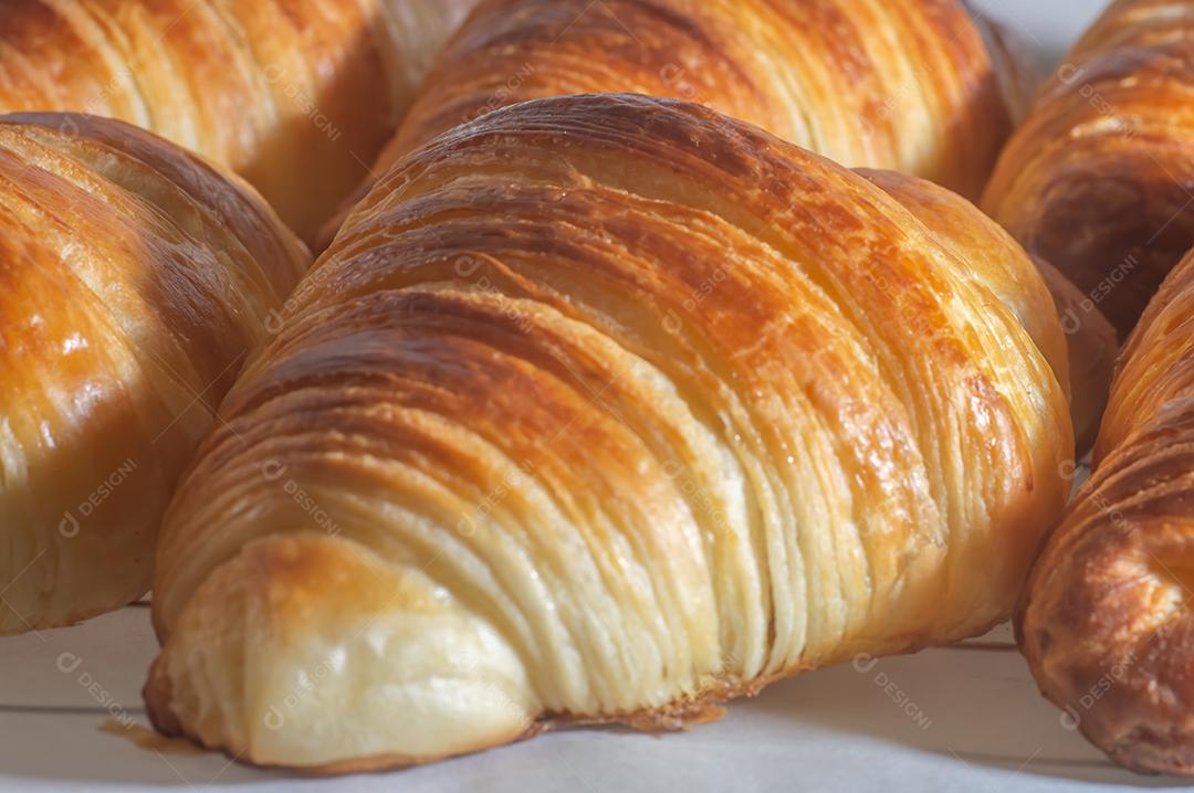 Deliciosos croissants caseiros em um papel manteiga branco, luz natural.