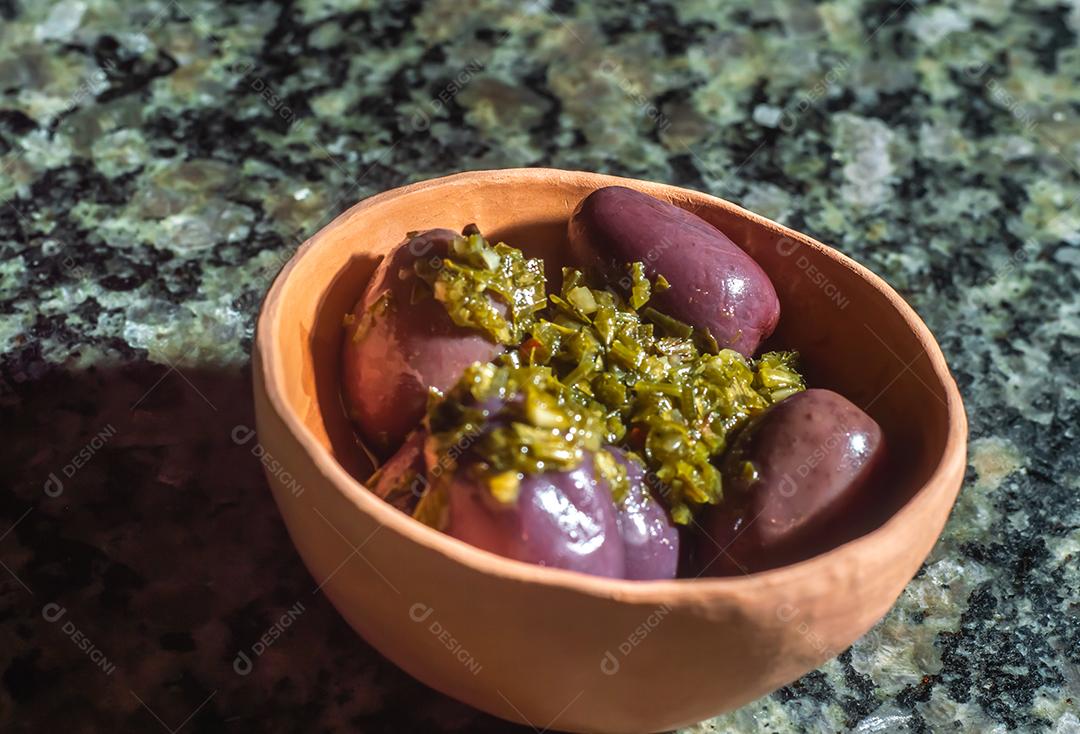 tigela com azeitonas e chimichurri em cima de uma mesa de marmore.