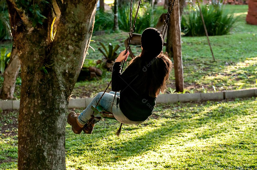 Garota no jardim balançando no balanço da árvore.