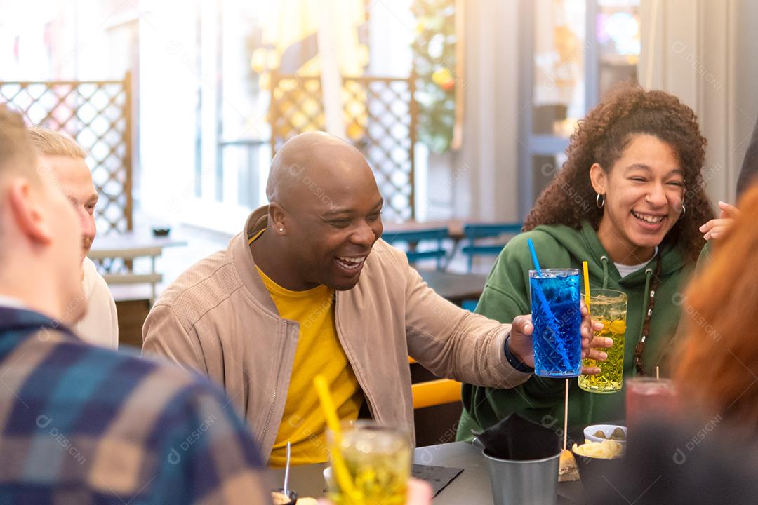 Grupo de amigos multirraciais felizes ri bebendo e comendo na reunião do restaurante - amizade multiétnica