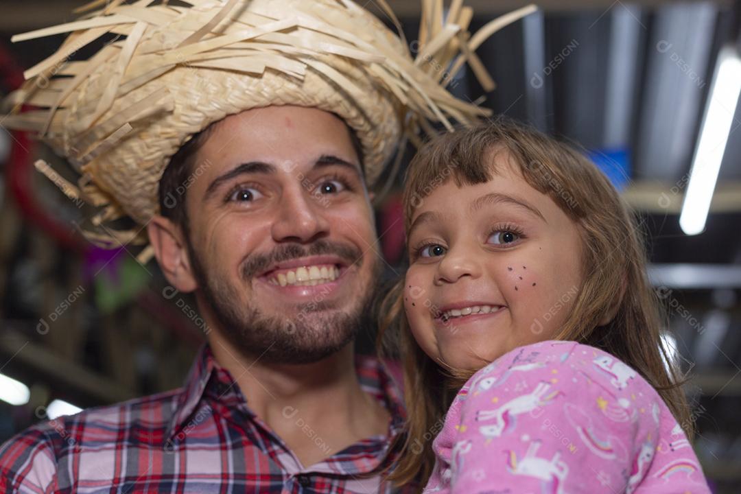 Homem bonito com roupas típicas da festa junina sorrindo com uma menina nos braços