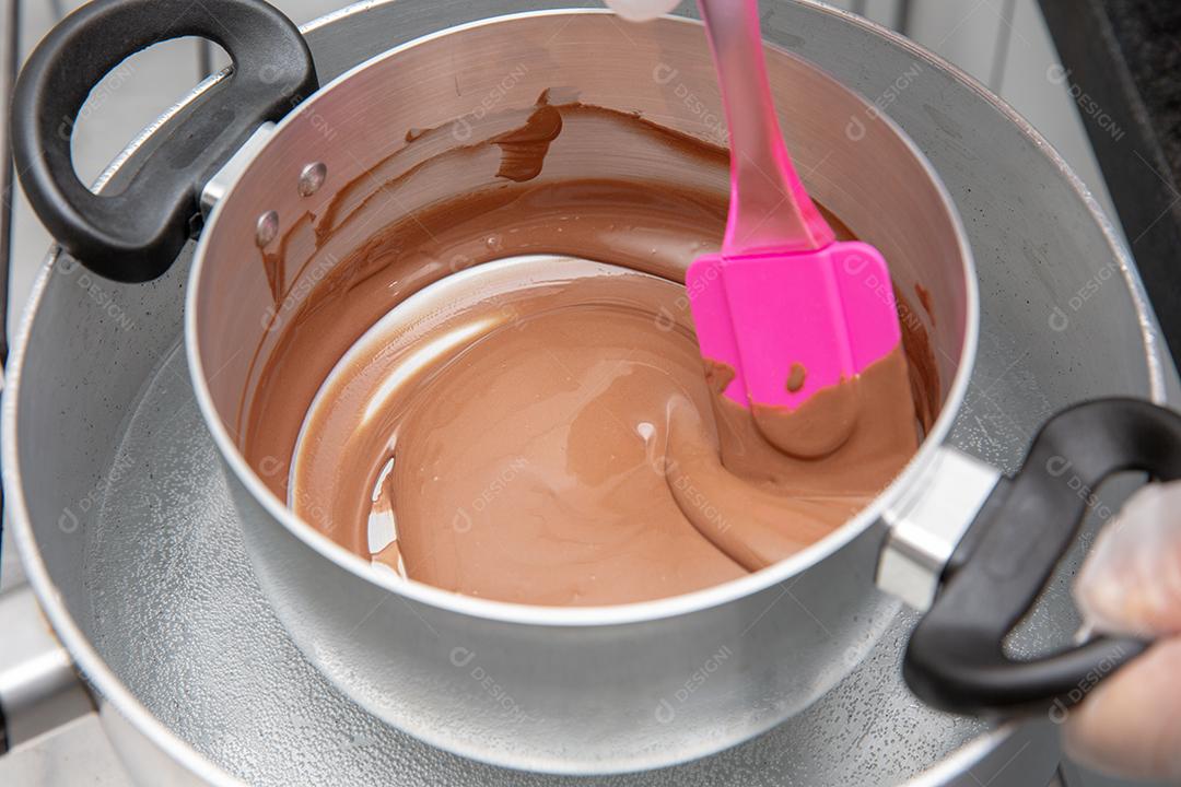 Panela com chocolate derretido sendo removido pela mão do chef