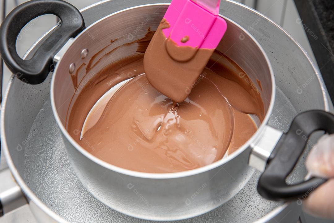 Panela com chocolate derretido sendo removido pela mão do chef