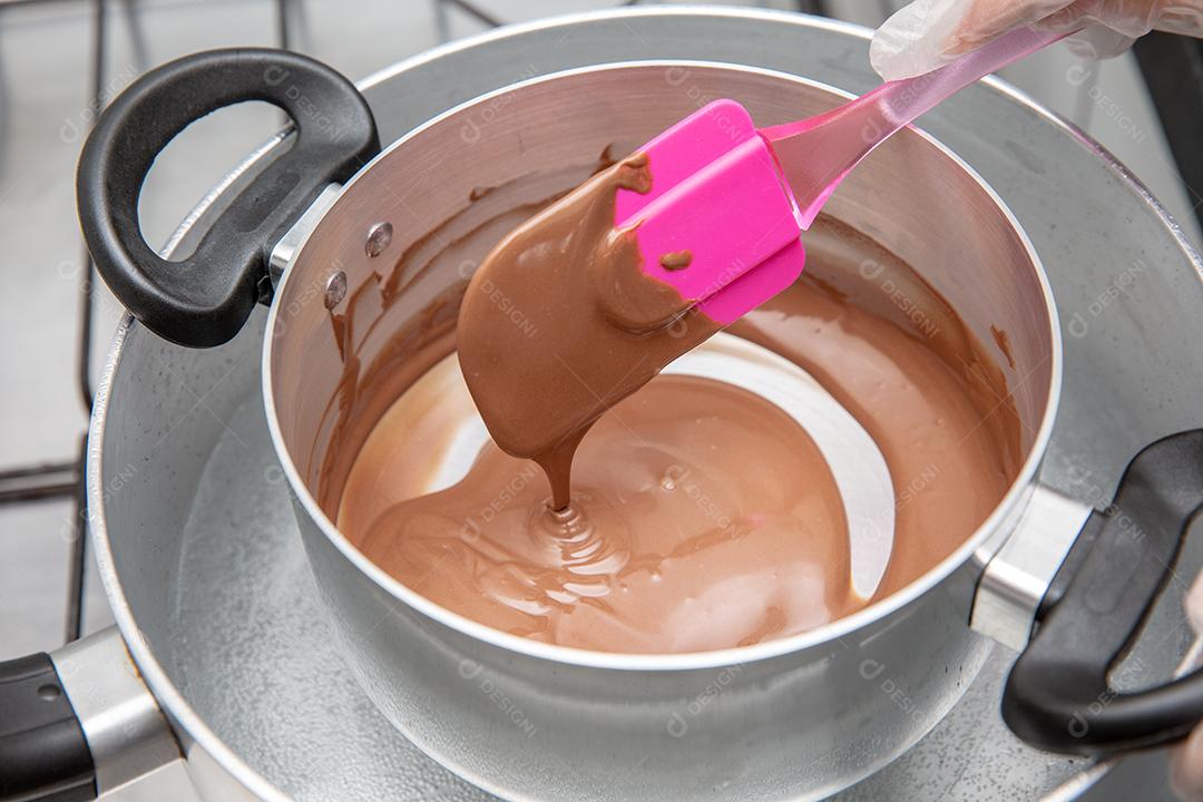 Panela com chocolate derretido sendo removido pela mão do chef