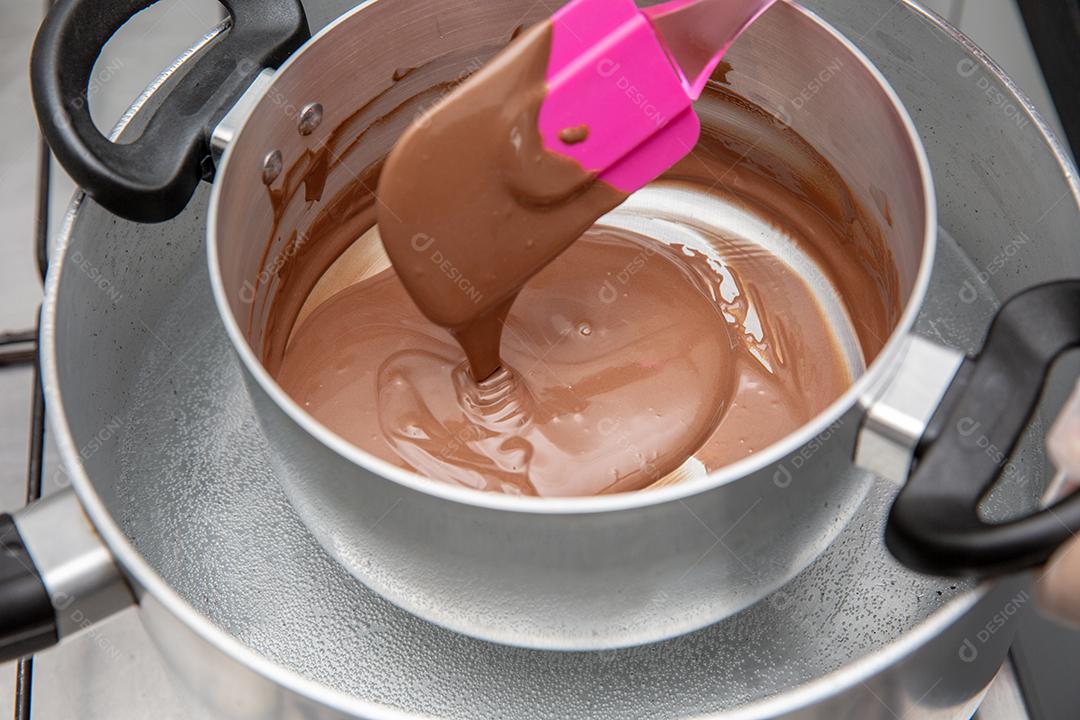 Panela com chocolate derretido sendo removido pela mão do chef