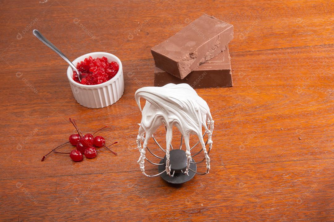 Batedor de metal com ovo batido com sombras brancas na mesa de madeira