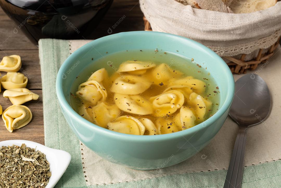 Sopa de tortellini brodo em uma tigela com fatias de pão e temperos sobre mesa de madeira