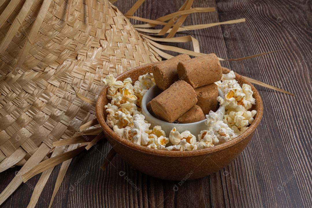 Pipoca, doce de amendoim servido em uma panela com chapéu de palha em mesa de madeira