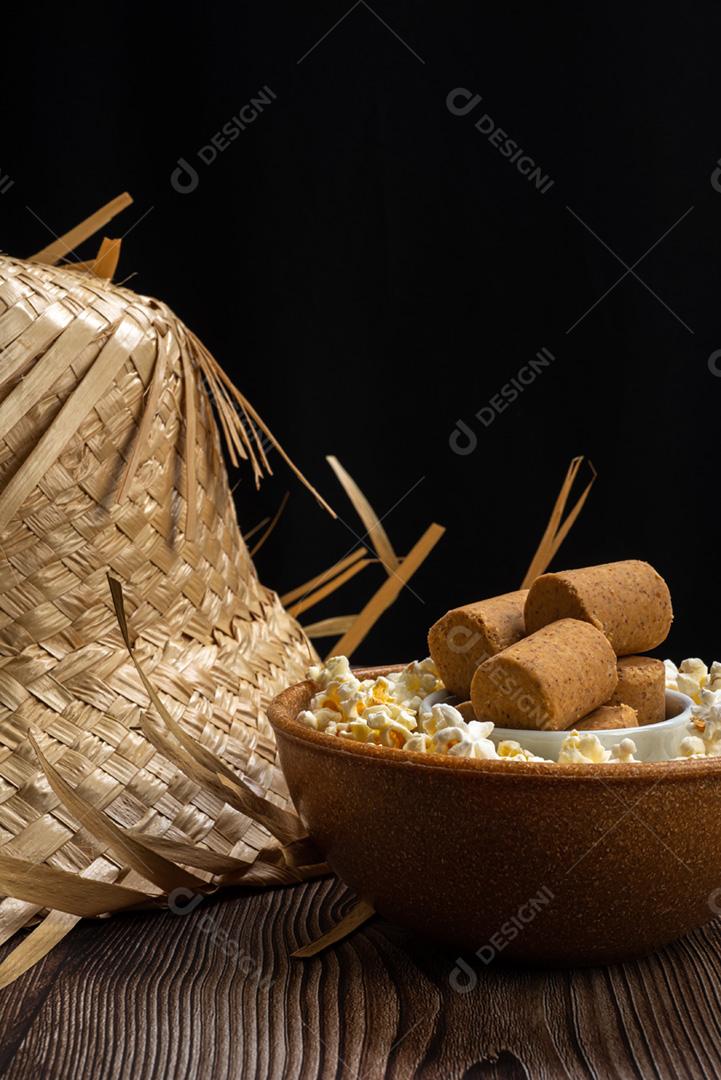 Pipoca, doce de amendoim servido em uma panela com chapéu de palha em mesa de madeira