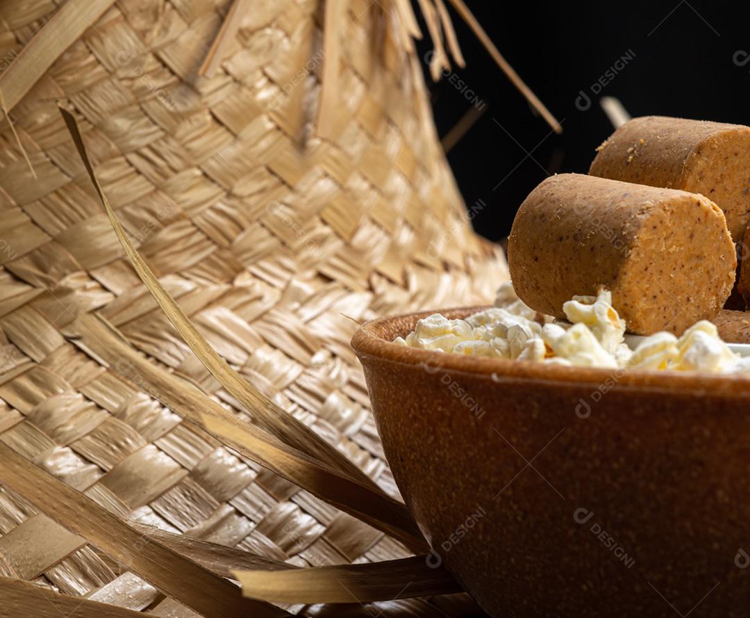 Pipoca, doce de amendoim servido em uma panela com chapéu de palha em mesa de madeira