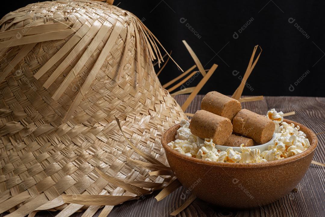 Pipoca, doce de amendoim servido em uma panela com chapéu de palha em mesa de madeira