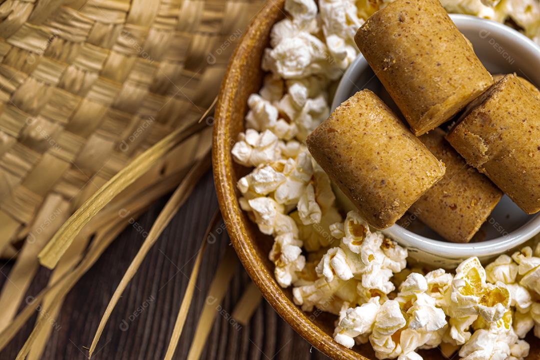 Pipoca, doce de amendoim servido em uma panela com chapéu de palha em mesa de madeira