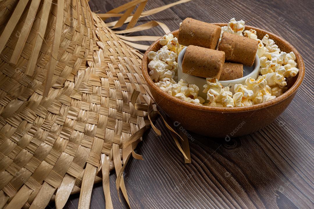 Pipoca, doce de amendoim servido em uma panela com chapéu de palha em mesa de madeira