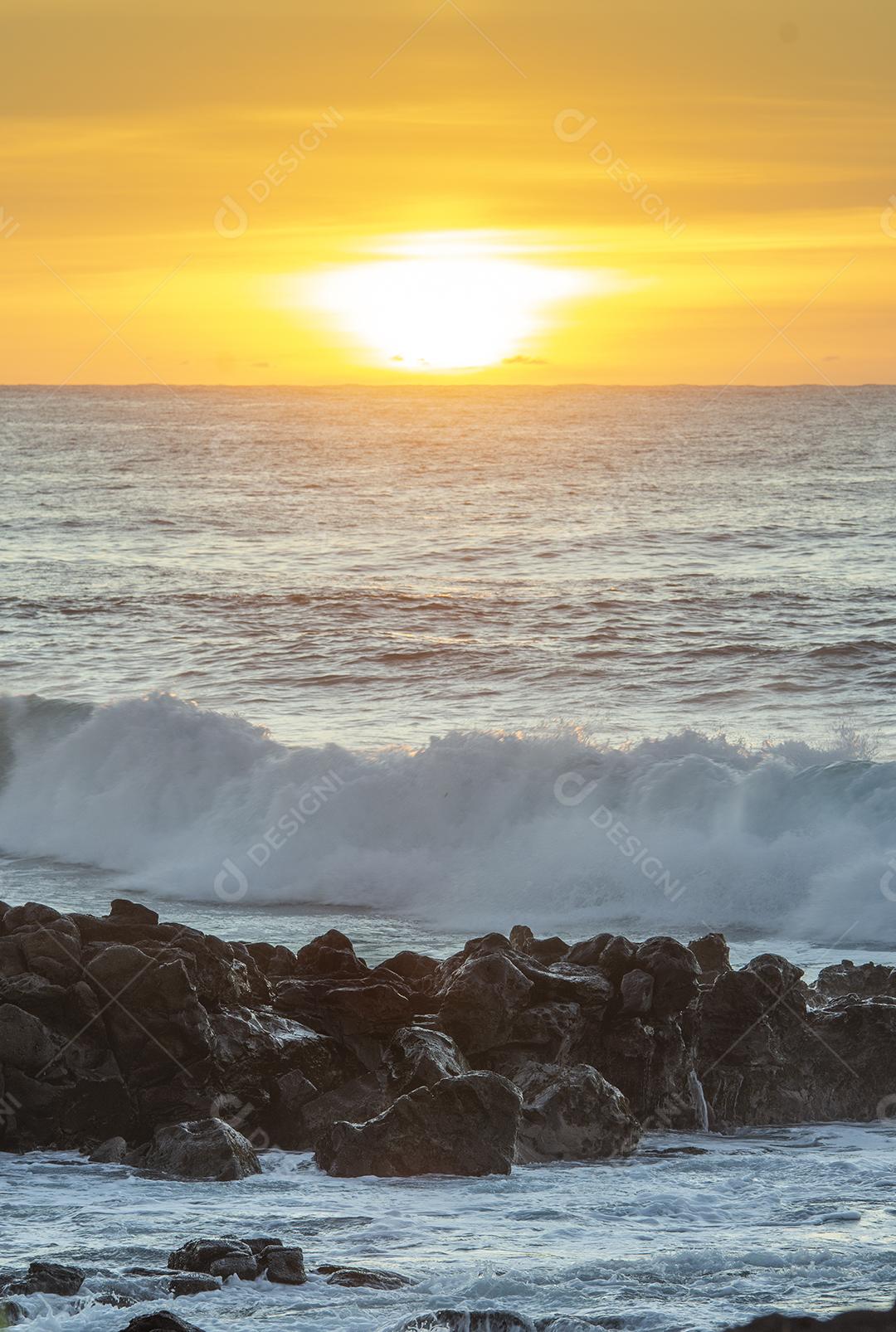 Pôr do sol sobre o mar na Ilha com pedras e ondas em beira mar