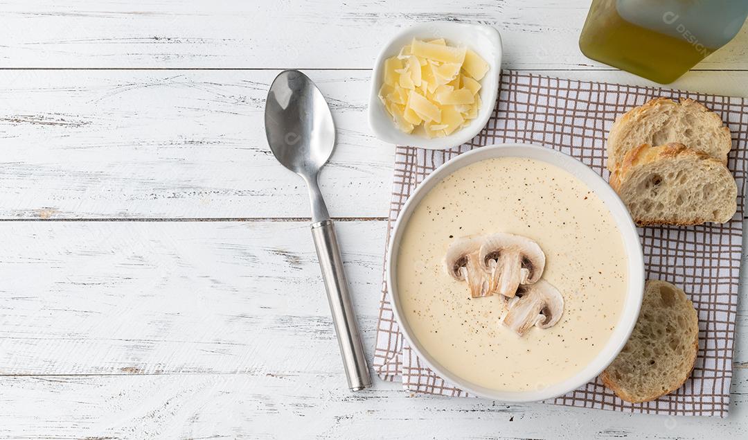 Sopa de cogumelos em uma tigela com fatias de pão e temperos sobre mesa de madeira