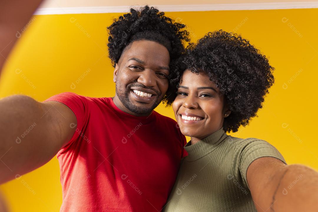 casal negro tirando uma selfie em fundo amarelo
