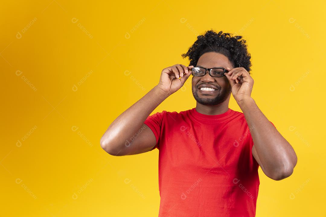 Homem afro com óculos em fundo amarelo sorrindo com a mao no oculos