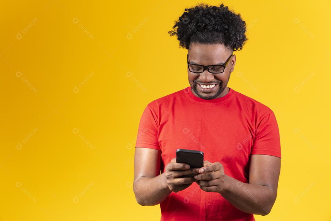 Homem afro com óculos em fundo amarelo sorrindo usando celular