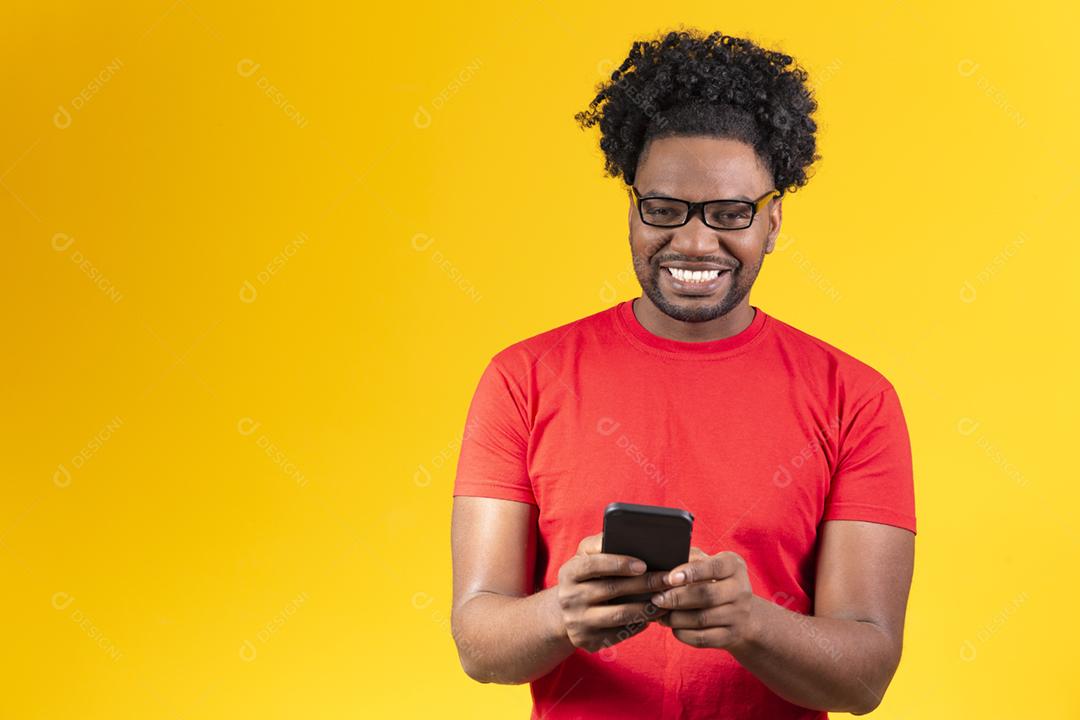 Homem afro com óculos em fundo amarelo sorrindo usando celular