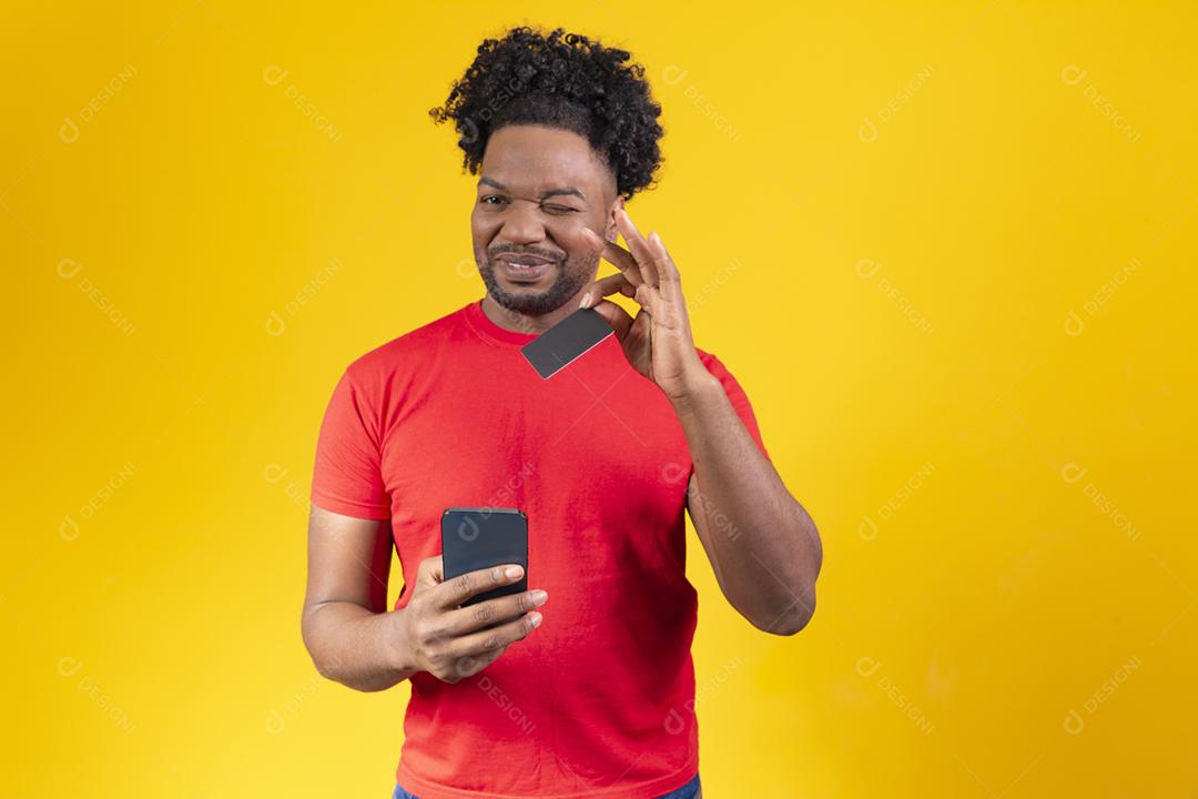 Alegre jovem afro segurando novo celular e um cartão de crédito