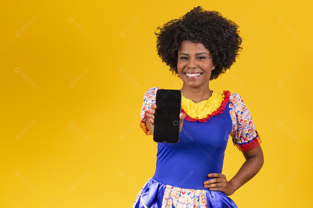 Mulher afro vestida com roupa de festa junina com um smartphone