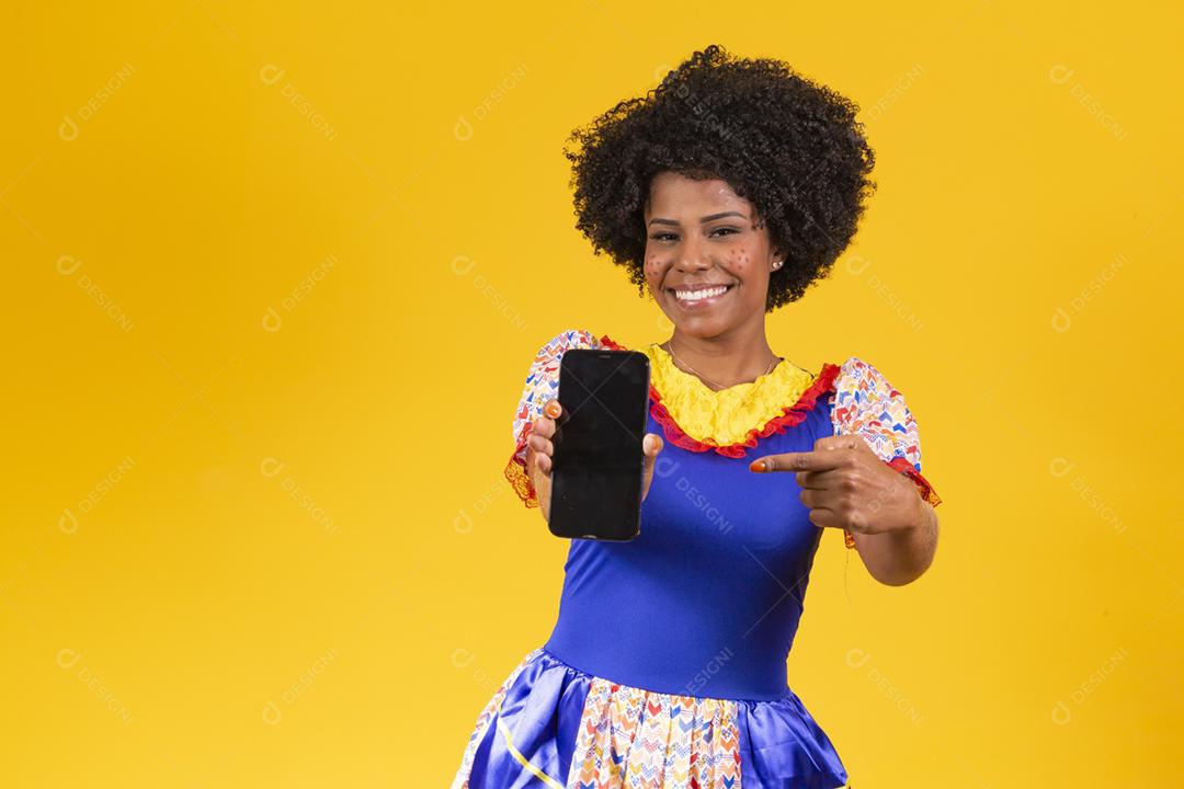 Mulher afro vestida com roupa de festa junina com um smartphone