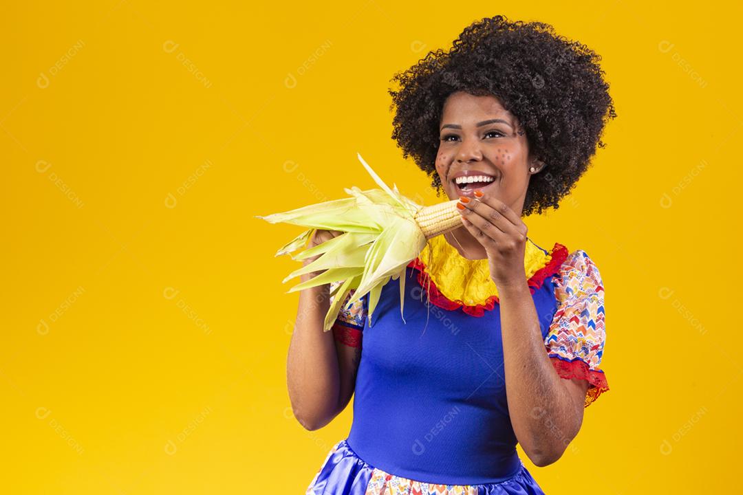 mulher bonita com roupas típicas da festa junina segurando um milho