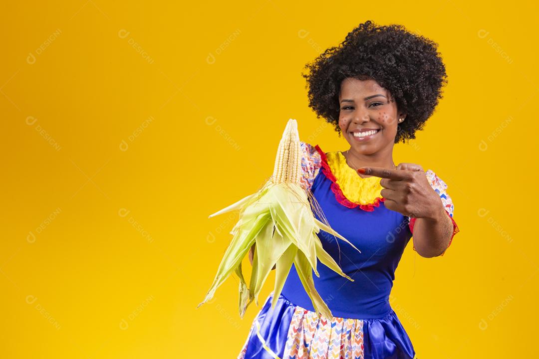 mulher bonita com roupas típicas da festa junina segurando um milho